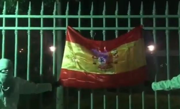 Dos jovenes sujetan la bandera española mientras comienza a arder./TWITTER