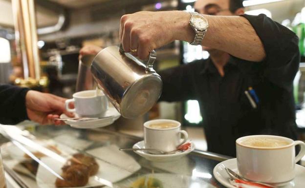 Un camarero sirve café en la barra de su bar./