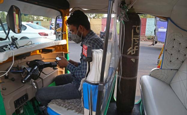 Khan consulta el móvil en su tuk-tuk medicalizado, con la bombona de oxígeno para el paciente./AFP