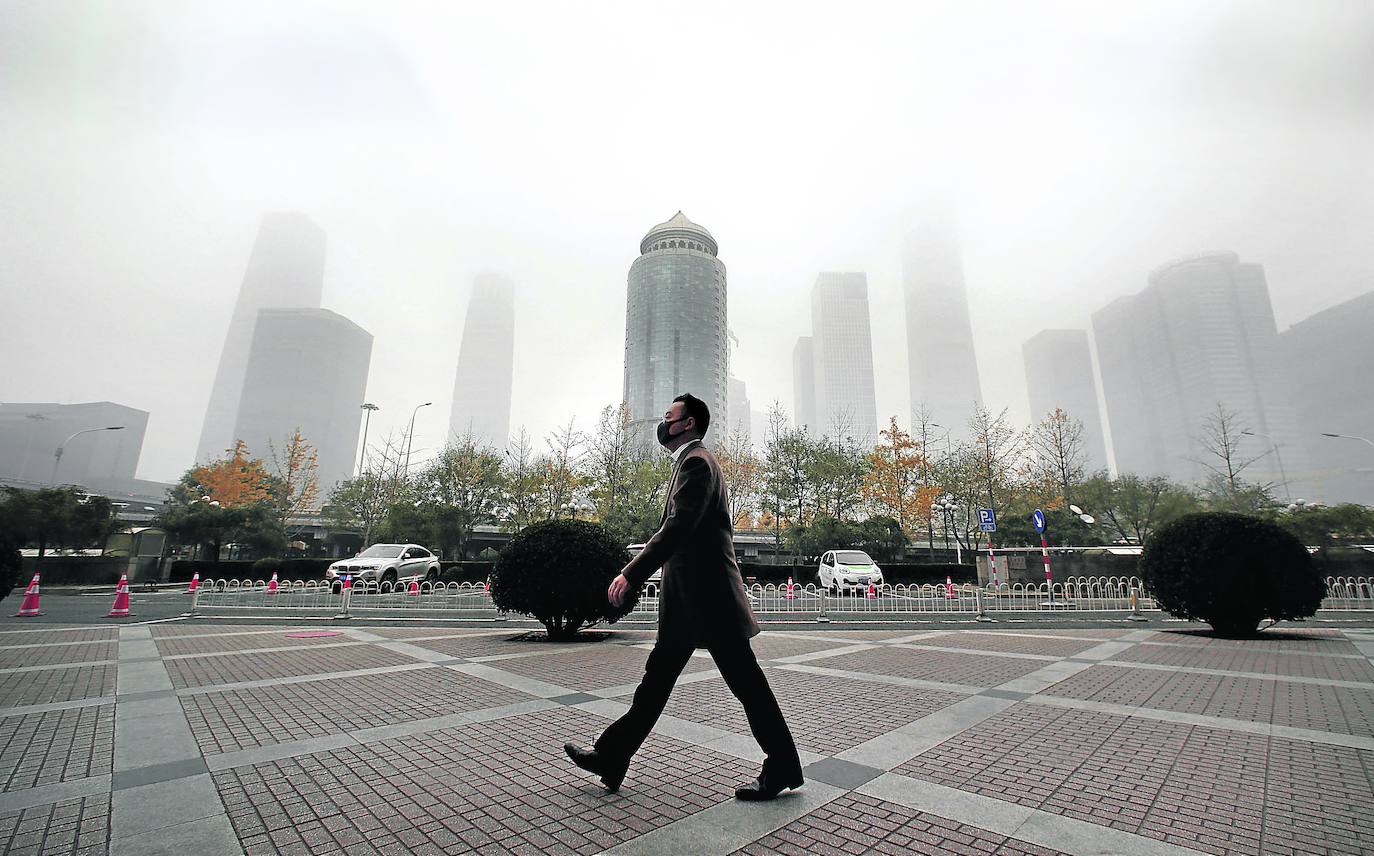 Un hombre camina por las calles de Pekín con la ciudad sumergida en una nube baja de contaminación./REUTERS