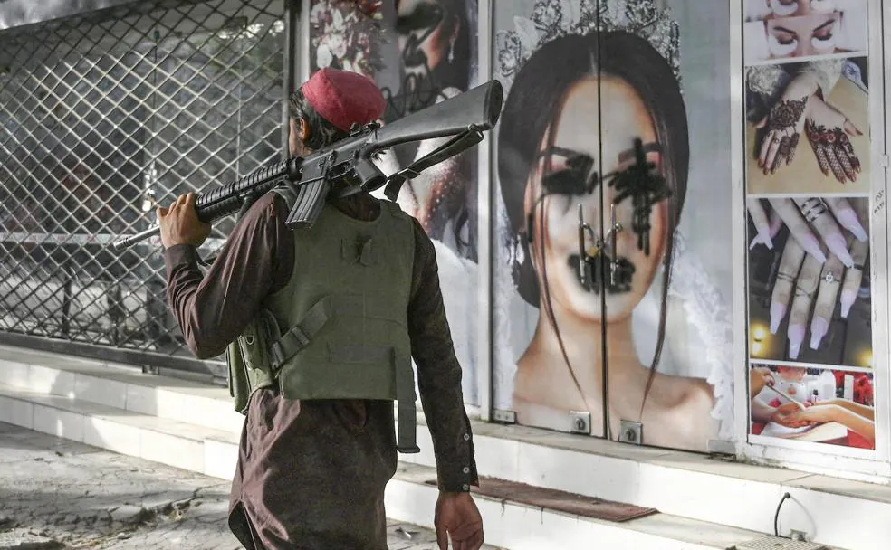 n talibán pasa frente a un salón de belleza en Kabul en el que han sufrido pintadas las fotos de mujeres./AFP